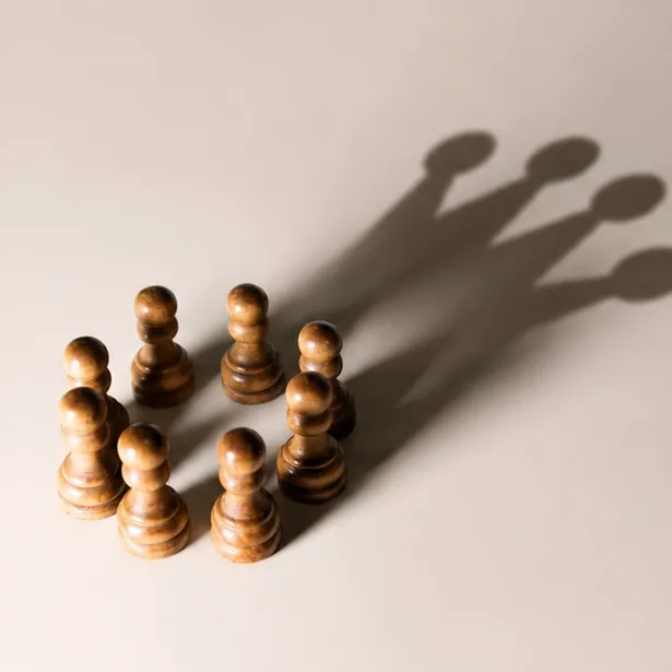 Mehrere Schachbauern werfen gemeinsam den Schatten einer Dame und symbolisieren Entwicklung und Führungspotenzial.