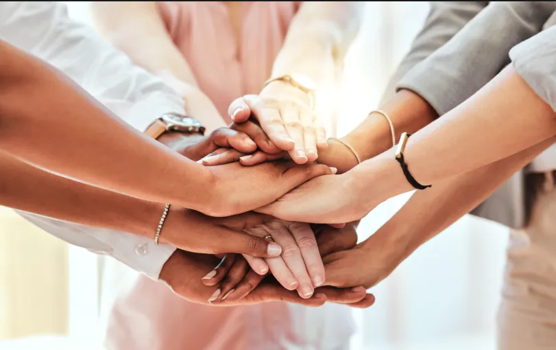 Verschiedene Hände liegen übereinander und symbolisieren Zusammenhalt und wirksame Teamarbeit.